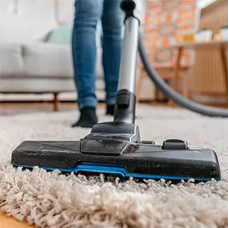 Vacuuming a living room rug during a recurring house cleaning